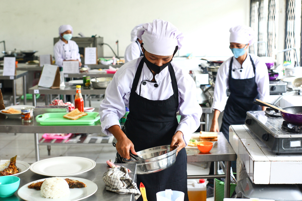 A Person in White Chef Hat and Black Apron Holding Stainless Steel Bowl